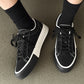 Black low-top sneakers with lace-up closures and white trim, side-by-side view