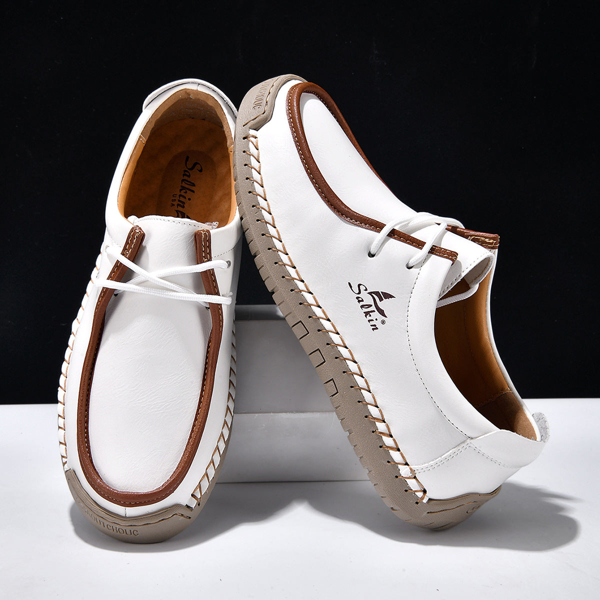 White lace-up casual shoes with brown trim and lace, stitched moccasin-style upper.