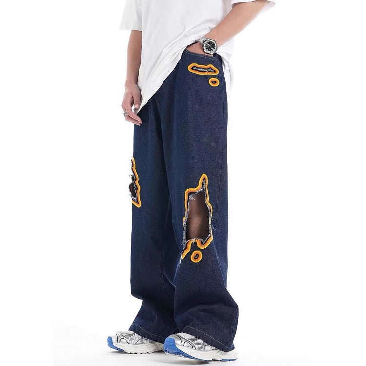 Loose dark denim trousers with large ripped embroidery patches on legs