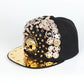 Black baseball cap with gold brim and ornate rhinestone skull face on side