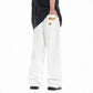 Loose white trousers with small ripped embroidery patch on the thigh